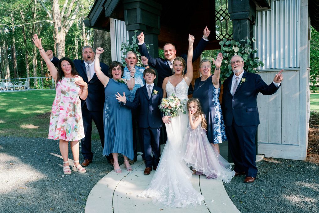 Family and wedding party cheering with raised arms outside the chapel