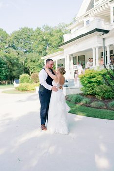 Bride and groom outside a white house with a wraparound porch