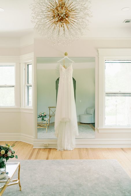 Wedding dress hanging in a bright room beneath a starburst chandelier
