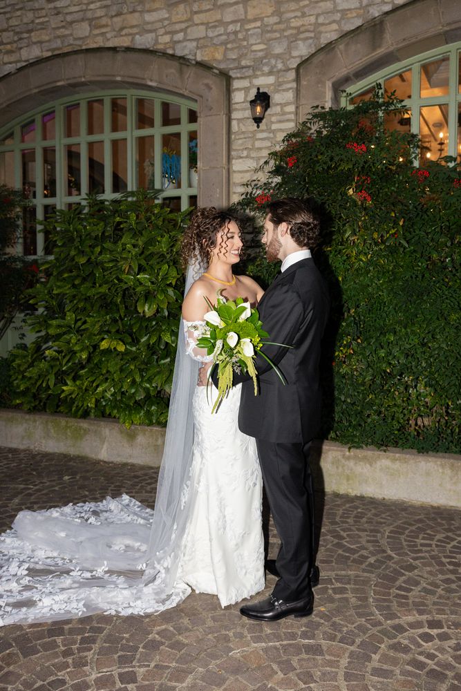 The couple together outside the venue at dusk, the bride's train spread on the stone