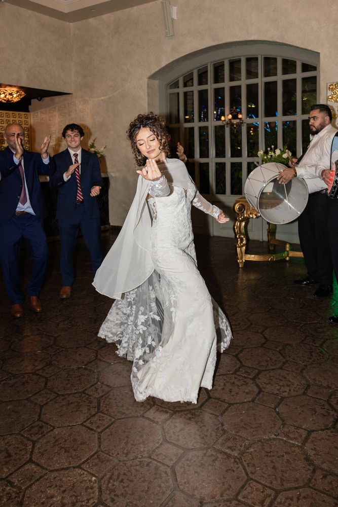 The bride dances as the guests clap and a drummer plays behind her