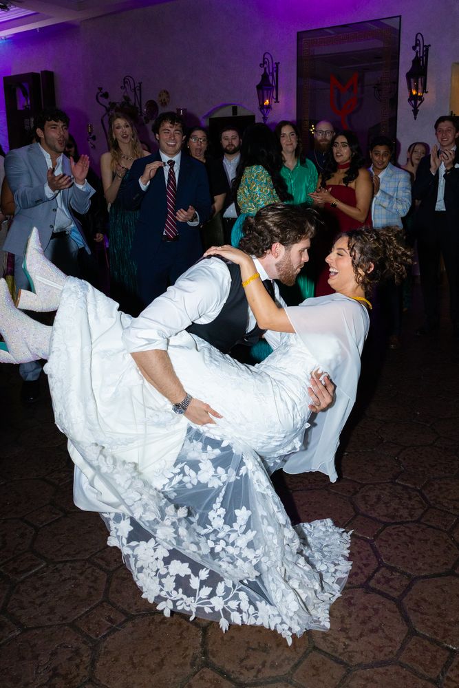 The groom dips the bride on the dance floor under purple light