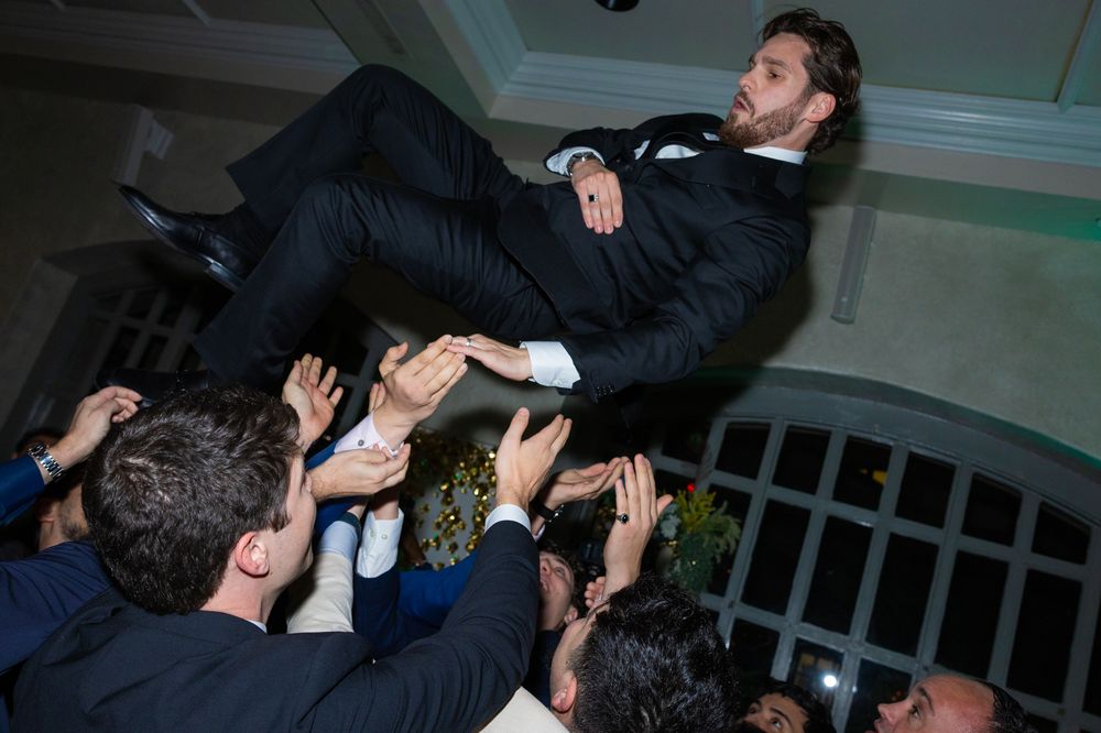 The groom is lifted overhead by a circle of guests
