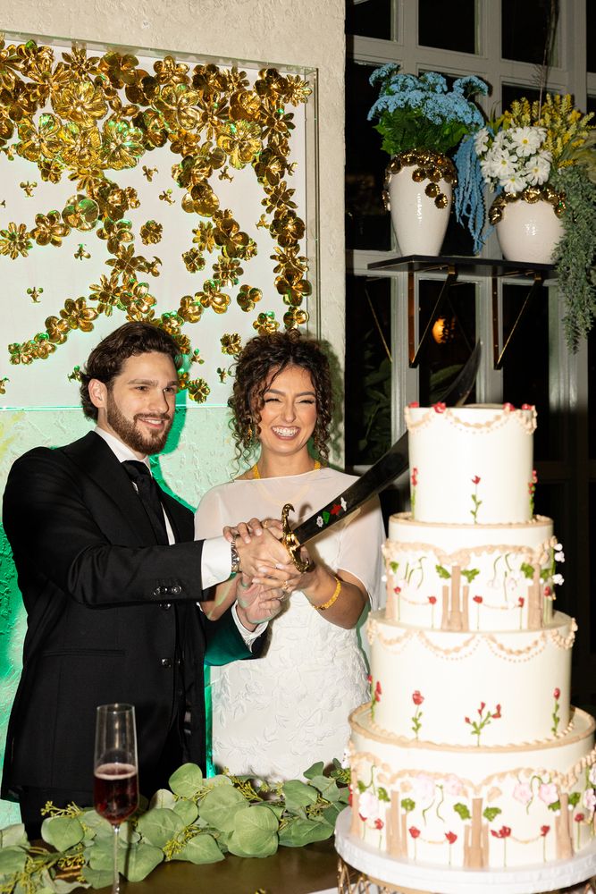 The couple cut the cake together, a knife in both their hands