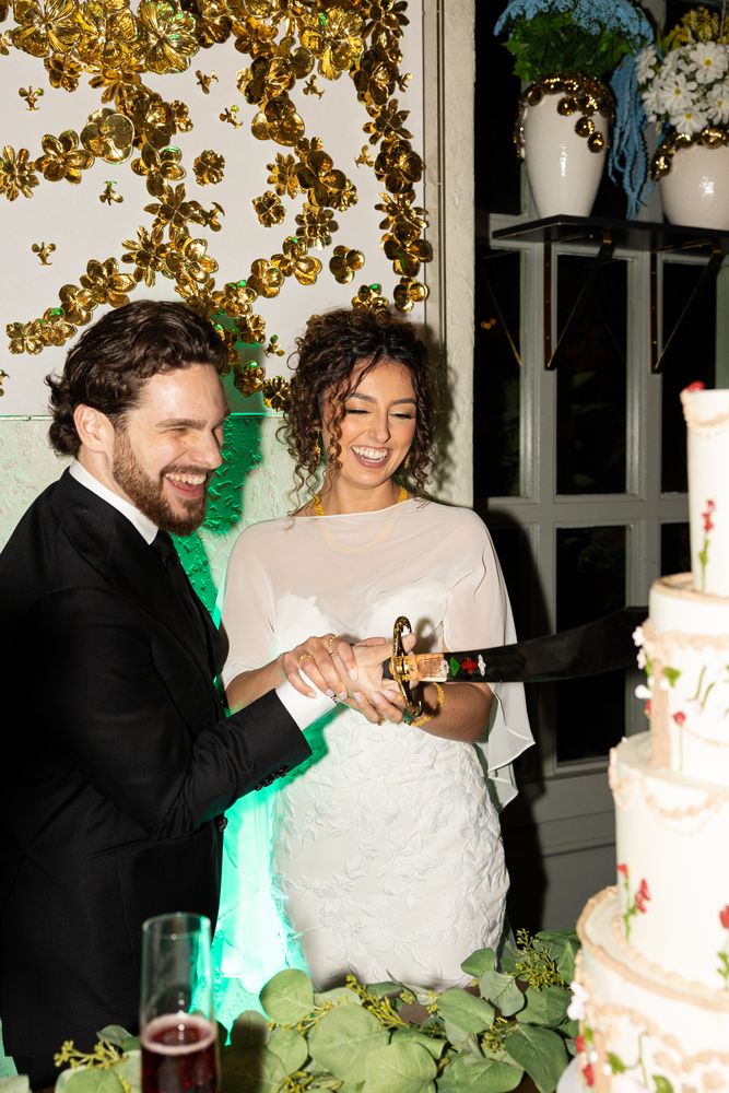 The couple laughing behind the cake as they cut the first slice