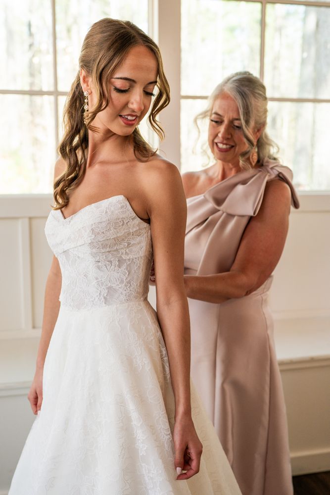 The bride being fastened into her gown beside a bright window