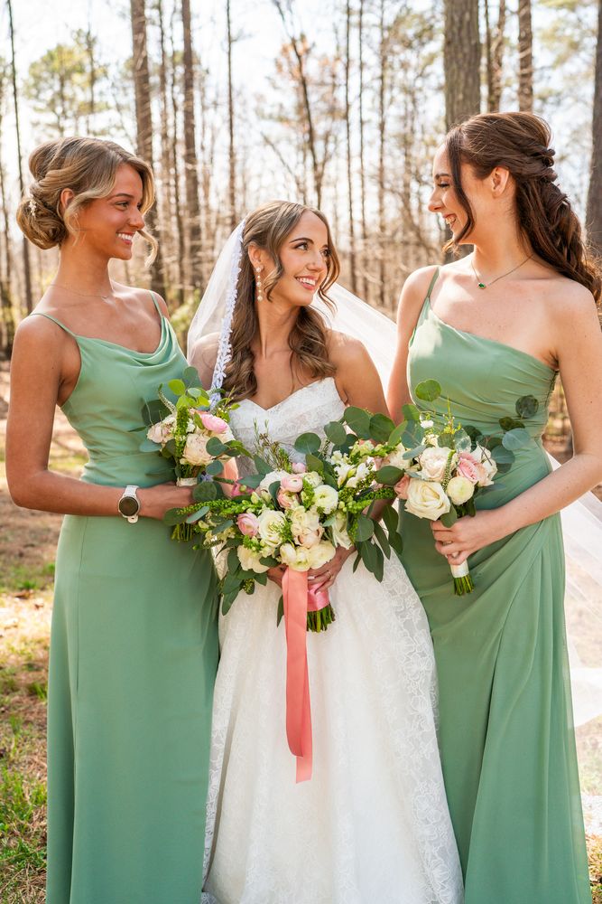 The bride between two bridesmaids in sage green, all holding bouquets