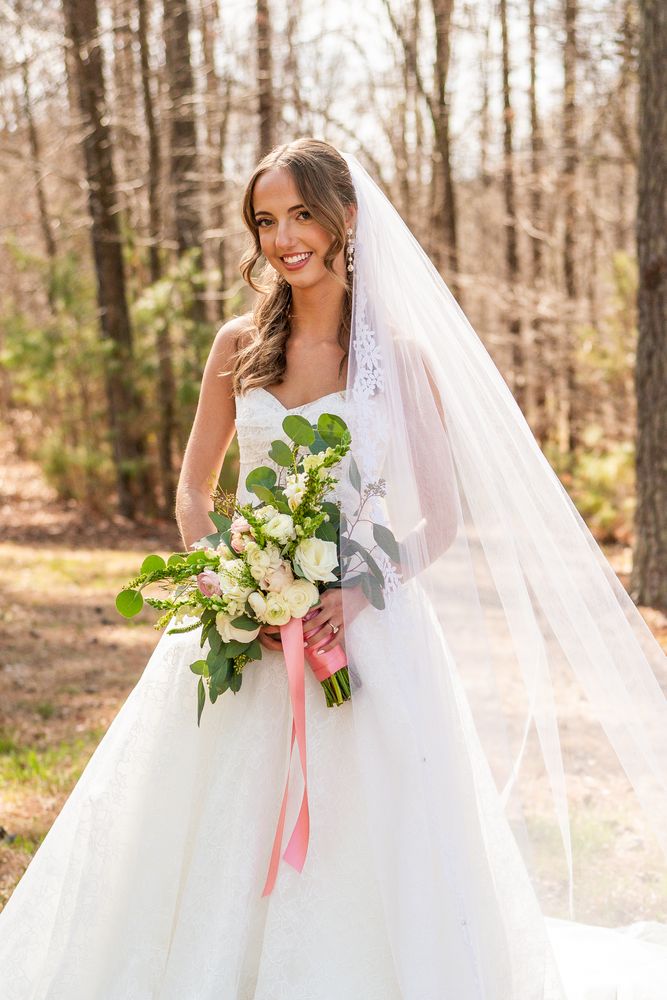 The bride among the pines holding a bouquet tied with coral ribbon