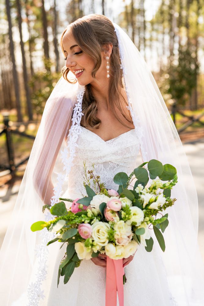 The bride smiling with her bouquet, veil over her shoulder