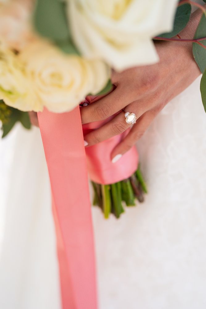 Close-up of the bride's ring hand resting on her bouquet's coral ribbon