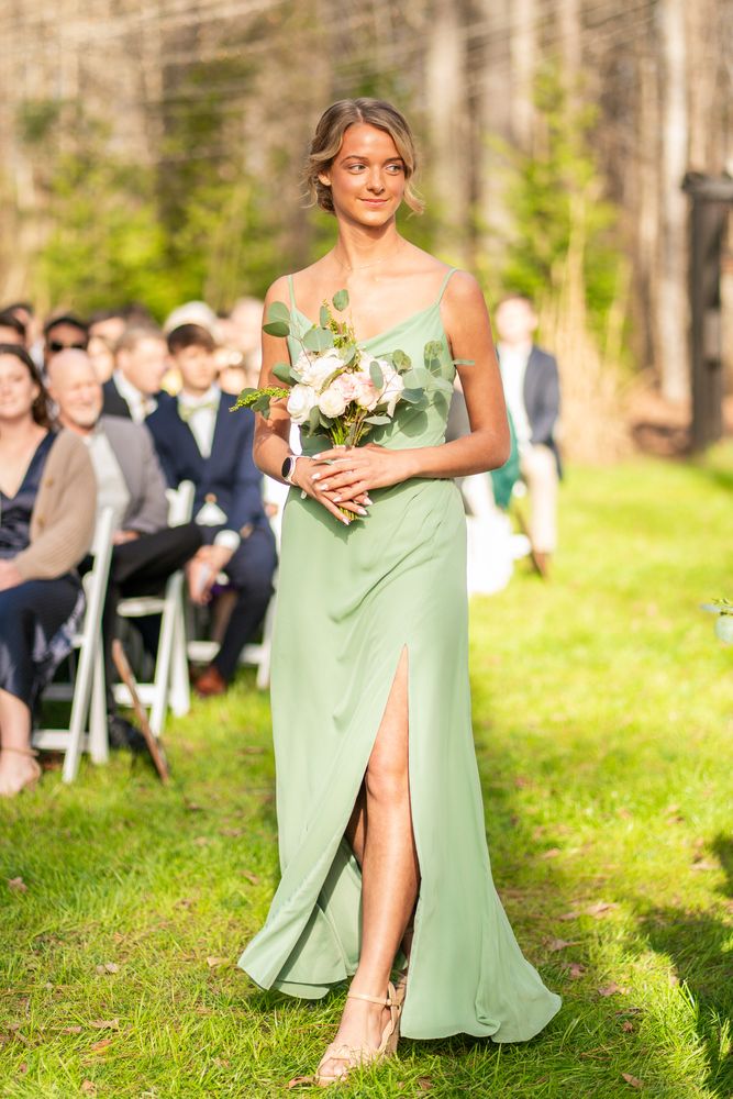 A bridesmaid in sage green walking the aisle between seated guests